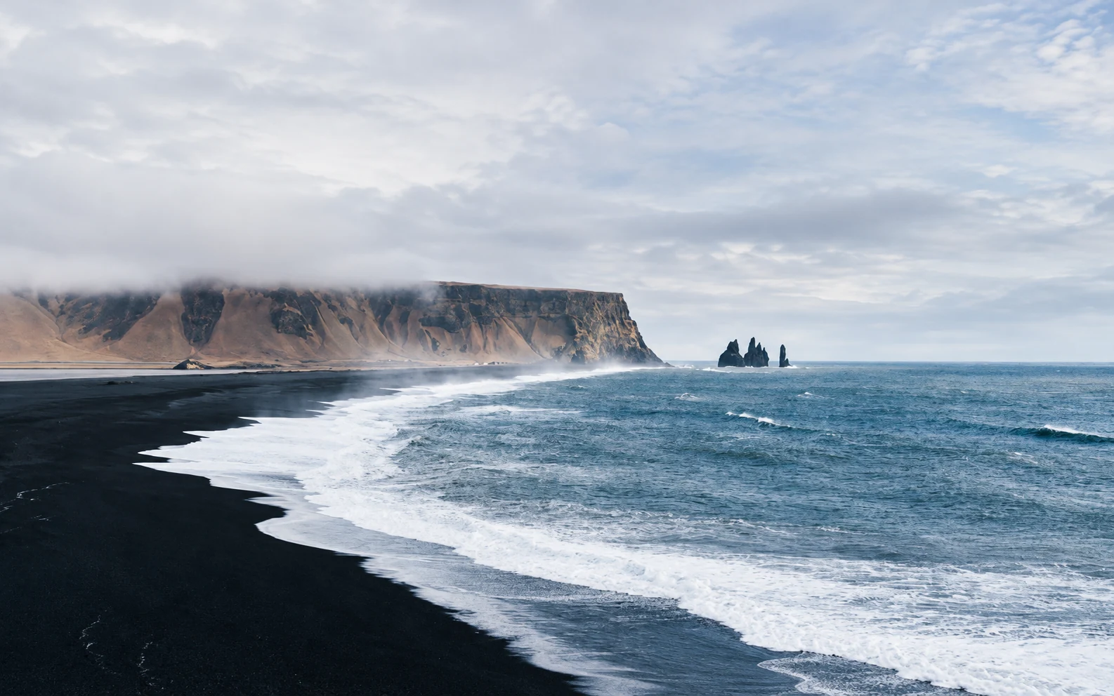 A black-sand beach below sea cliffs